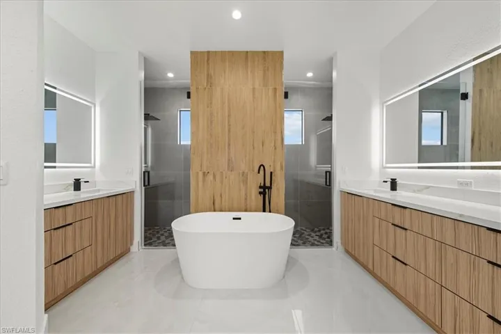 Bathroom featuring a stall shower, two vanities, a freestanding bath, and recessed lighting