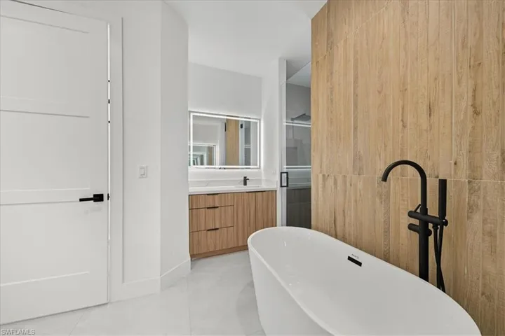 Bathroom featuring vanity, a freestanding tub, light tile patterned flooring, and a stall shower