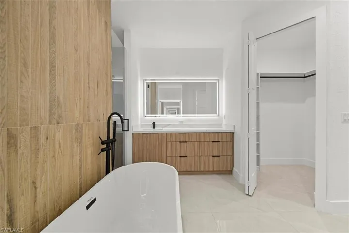 Bathroom with a spacious closet, light tile patterned floors, vanity, a soaking tub, and a shower stall