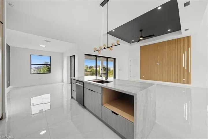 Kitchen featuring modern cabinets, open floor plan, light stone countertops, a raised ceiling, and decorative light fixtures