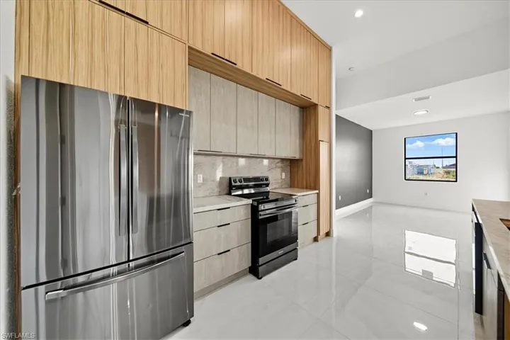 Kitchen with stainless steel appliances, modern cabinets, light brown cabinetry, recessed lighting, and light stone countertops