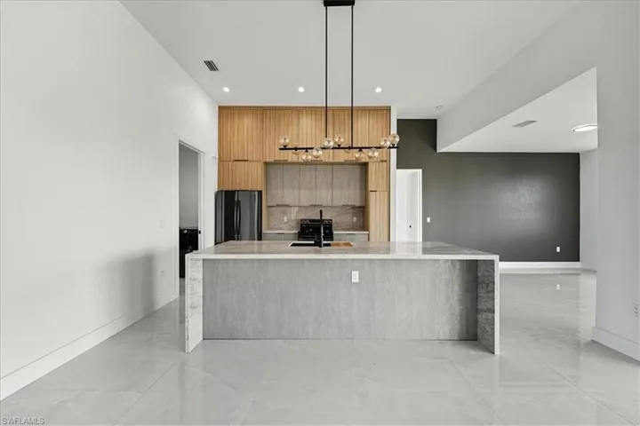 Kitchen with modern cabinets, light stone countertops, a spacious island, freestanding refrigerator, and hanging light fixtures