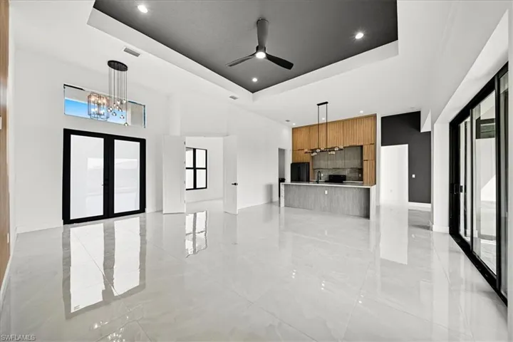 Unfurnished living room featuring a chandelier, healthy amount of natural light, a raised ceiling, french doors, and recessed lighting