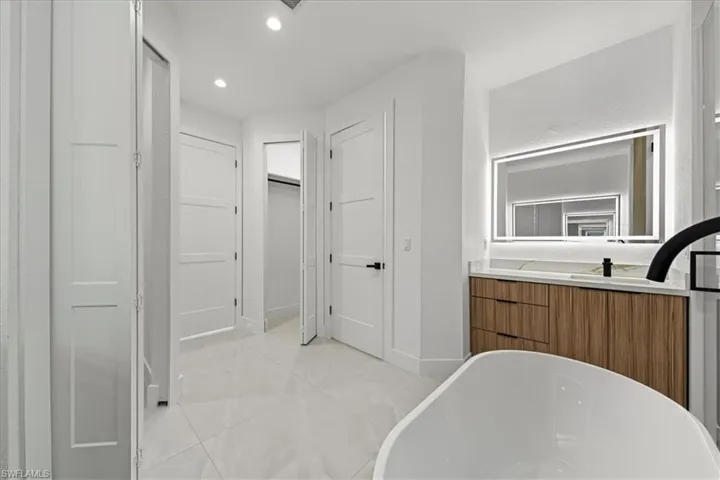 Bathroom featuring a freestanding tub, vanity, light tile patterned floors, a walk in closet, and recessed lighting