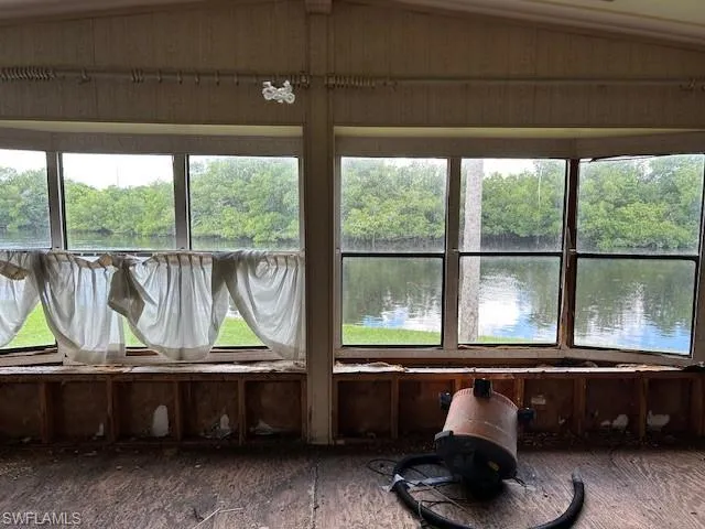 Sunroom with a water view, healthy amount of natural light, view of scattered trees, and lofted ceiling