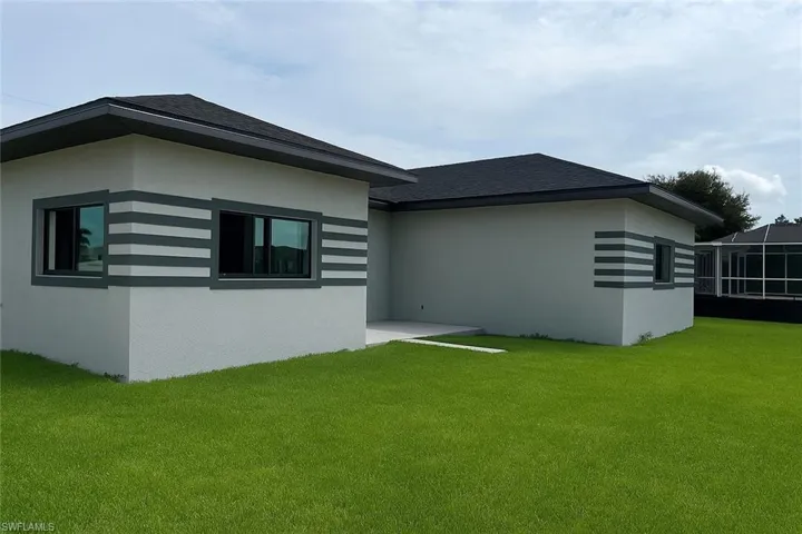Rear view of property featuring a lawn, stucco siding, and a shingled roof