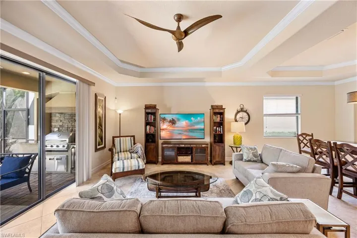 Living room featuring ornamental molding, a raised ceiling, light tile patterned floors, and ceiling fan