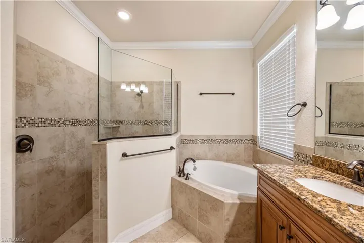 Full bath with vanity, ornamental molding, a garden tub, and a walk in shower