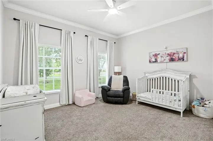 Carpeted bedroom with a crib, crown molding, and ceiling fan