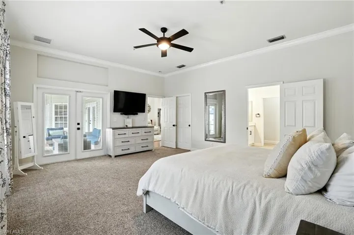 Bedroom with crown molding, light colored carpet, french doors, a ceiling fan, and connected bathroom