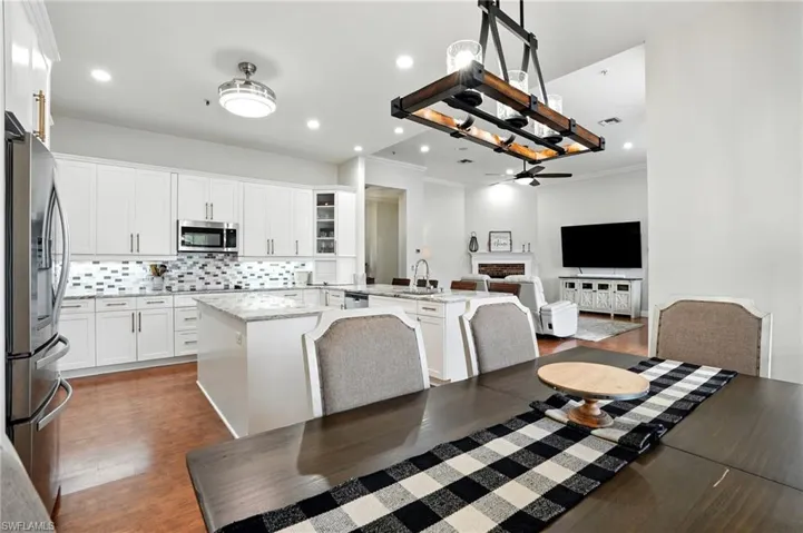 Kitchen with a center island with sink, stainless steel appliances, backsplash, decorative light fixtures, and white cabinetry