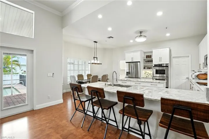 Kitchen featuring decorative backsplash, white cabinetry, light stone counters, pendant lighting, and a kitchen bar