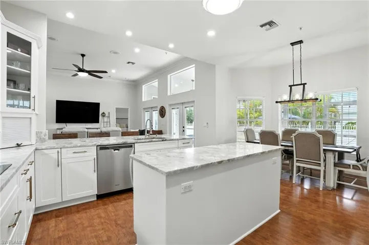 Kitchen with white cabinetry, glass insert cabinets, decorative light fixtures, stainless steel dishwasher, and light stone countertops