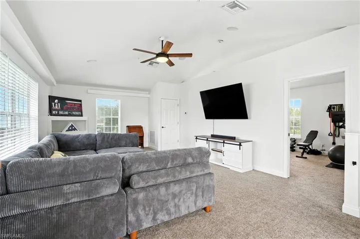 Living area featuring lofted ceiling, light carpet, and ceiling fan