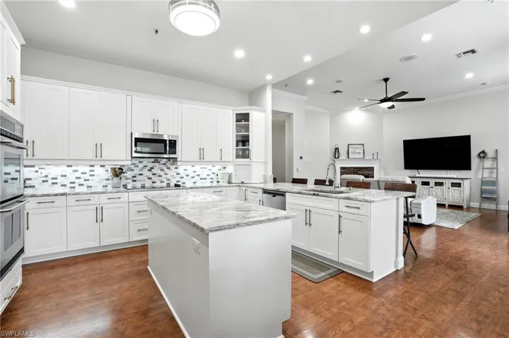 Kitchen featuring a center island, white cabinets, decorative backsplash, crown molding, and a brick fireplace