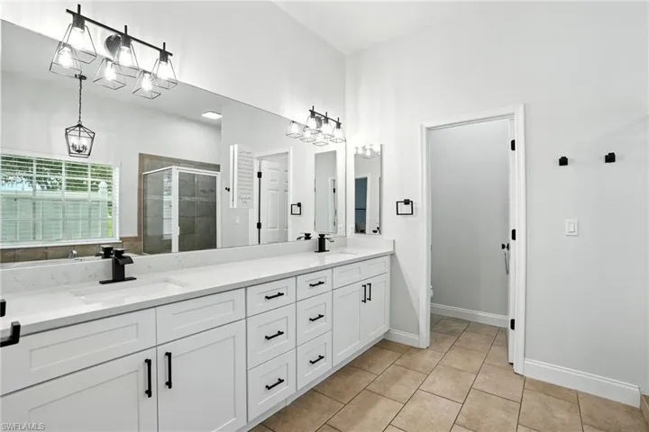 Full bath featuring a shower stall, double vanity, and light tile patterned flooring
