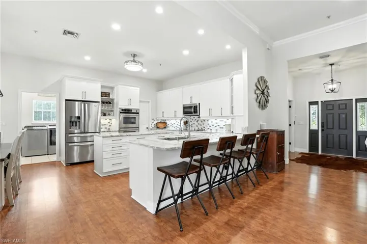 Kitchen with a kitchen breakfast bar, backsplash, white cabinets, stainless steel appliances, and recessed lighting