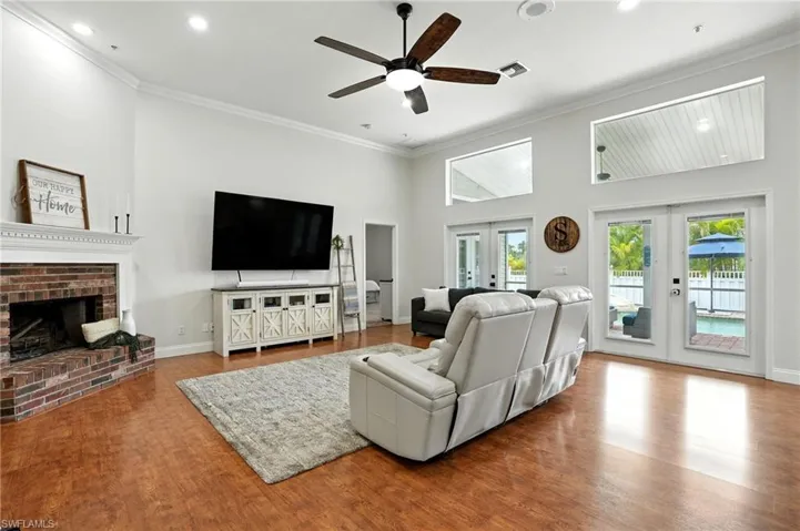 Living room with a fireplace, crown molding, wood finished floors, french doors, and a high ceiling