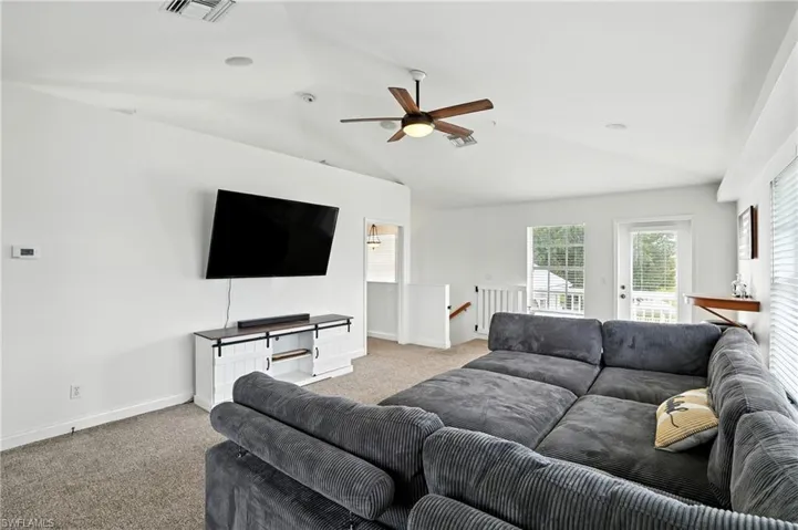 Living area with vaulted ceiling, carpet flooring, and ceiling fan