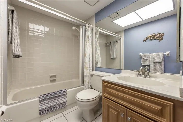 Bathroom featuring a tub/shower combination with white subway tile surround, white tile flooring, wood-finish vanity with a white countertop, and a large wall-mounted mirror