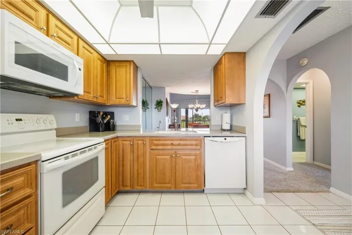 Kitchen featuring white tile flooring, honey-toned cabinetry, white appliances, and light-toned countertops