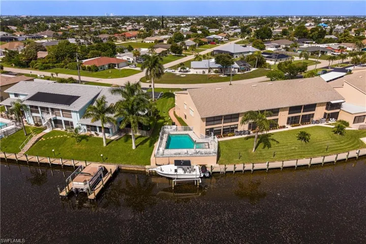 Waterfront property featuring a private boat dock, adjacent swimming pool, and mature palm trees