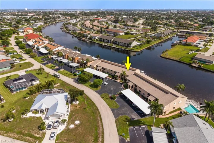 Waterfront condominium building featuring multiple boat slips, an in-ground swimming pool, and dedicated carport parking