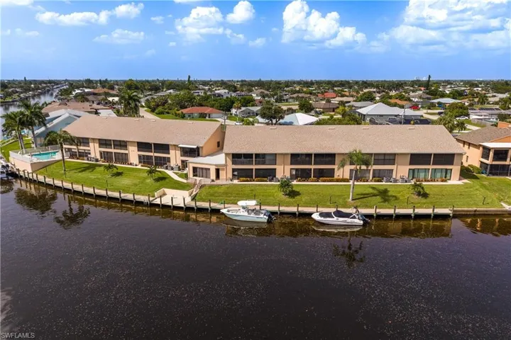 Waterfront condominium complex featuring a dock, mature palm trees, a swimming pool, and screened balconies