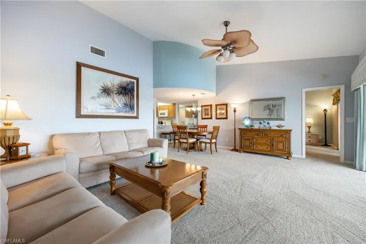 Open-concept living space with vaulted ceilings, light-toned carpeting, and a ceiling fan