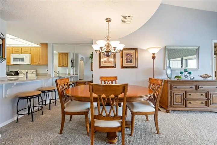 Carpeted dining area featuring a chandelier, a breakfast bar, light wood cabinetry, and mirrored wall panels