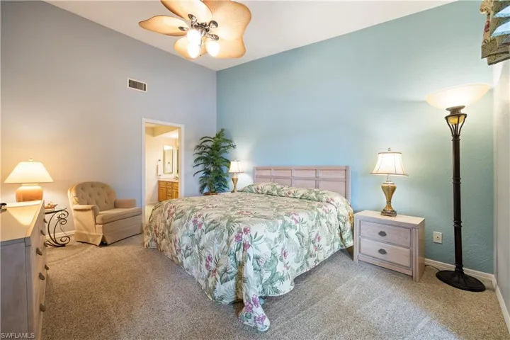 Vaulted ceilings accent this carpeted bedroom featuring a light wood-finish headboard and two-tone wall paint