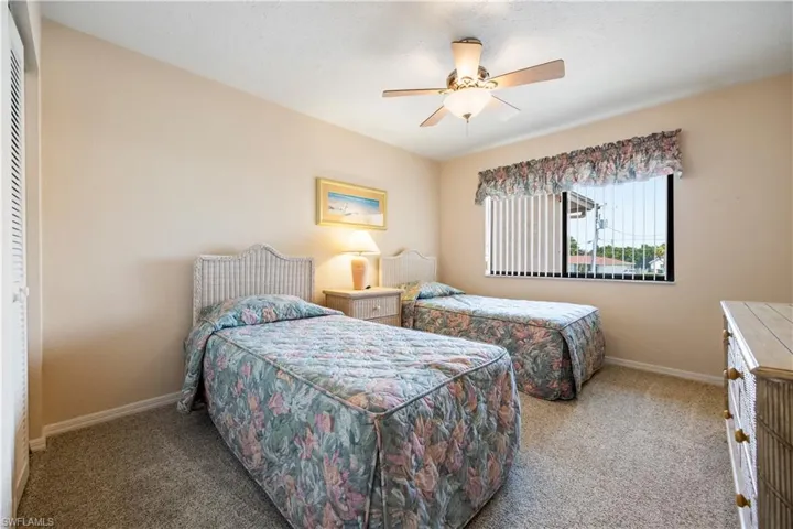 Carpeted interior space featuring a window with vertical blinds, a ceiling fan with integrated lighting, and a louvered bi-fold door