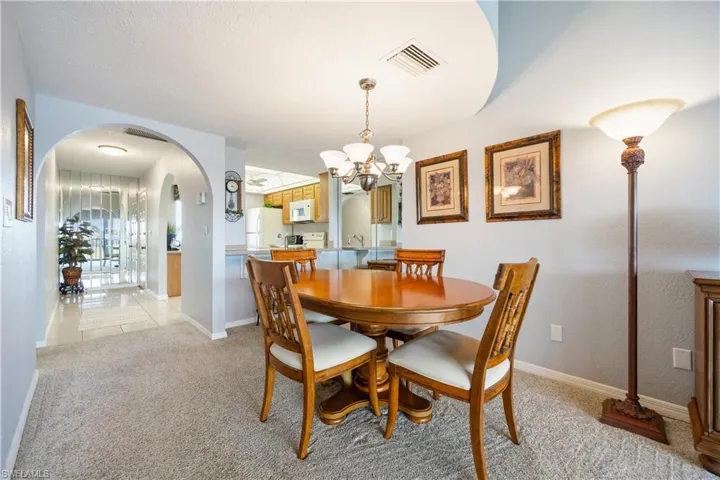 Carpeted dining area featuring a chandelier, a breakfast bar, and arched doorways