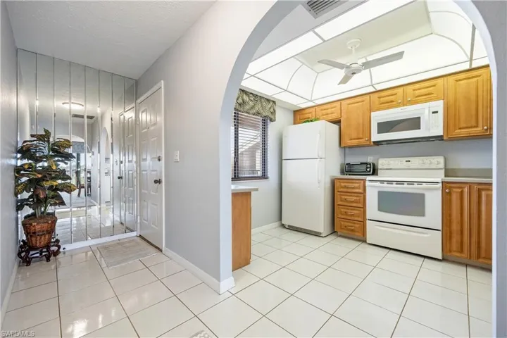Kitchen featuring wood-finish cabinetry, white appliances, and a tray ceiling with a flush-mount light