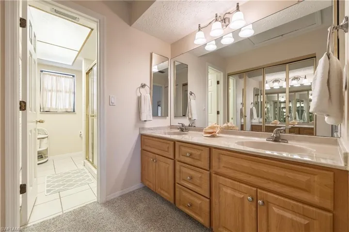 Bathroom featuring a double vanity with light wood cabinetry, dual integrated sinks, and an extended mirror
