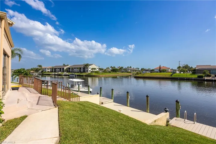Waterfront canal property featuring a private dock with pilings, a concrete seawall, and a wooden waterside deck with steps