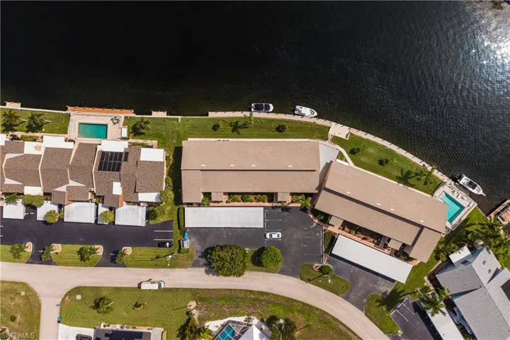 Waterfront property featuring multiple buildings with tan roofs, covered parking areas, and two swimming pools
