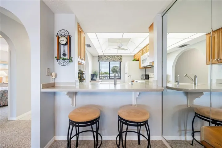 Kitchen pass-through featuring a light-toned countertop, wood-finish cabinetry, white appliances, and a ceiling fan