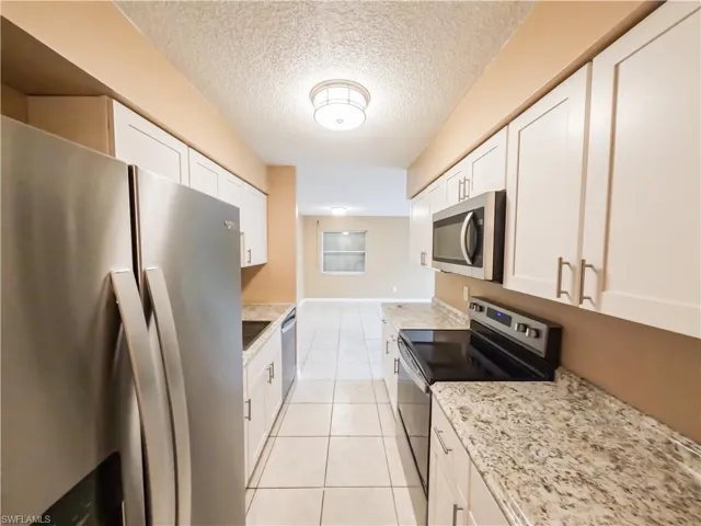 Kitchen featuring stainless steel appliances, a textured ceiling, light stone counters, light tile patterned floors, and white cabinets