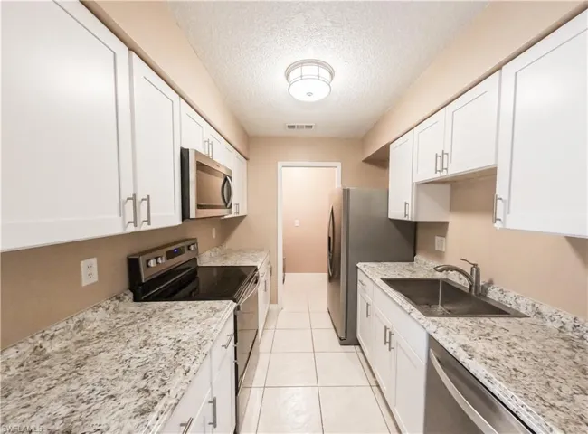 Kitchen featuring appliances with stainless steel finishes, white cabinets, light stone counters, a textured ceiling, and light tile patterned flooring