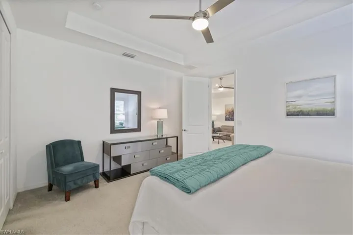 Carpeted bedroom featuring a tray ceiling and a ceiling fan