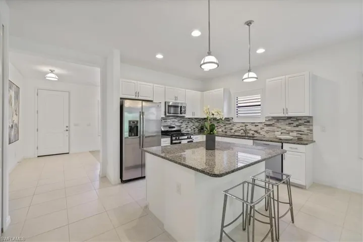 Kitchen featuring a breakfast bar, stainless steel appliances, white cabinets, pendant lighting, and dark stone counters