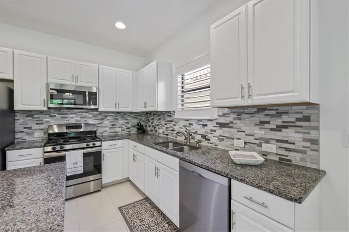 Kitchen with stainless steel appliances, white cabinets, dark stone counters, light tile patterned floors, and recessed lighting
