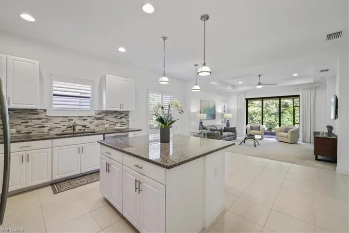 Kitchen with dark stone countertops, decorative light fixtures, white cabinets, a center island, and open floor plan
