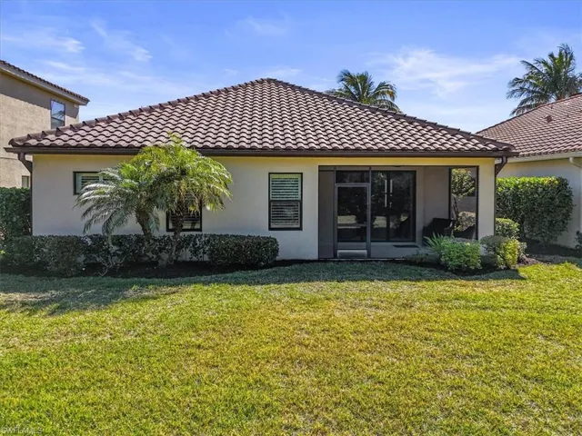 Rear view of house featuring stucco siding, a yard, and a tile roof
