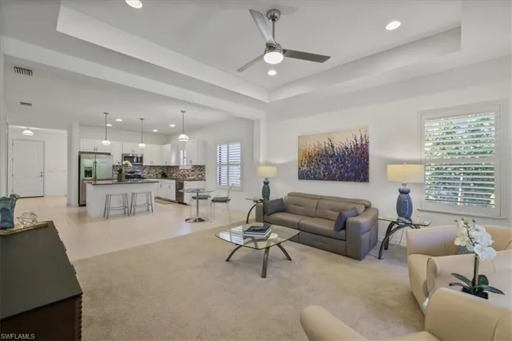Living area with a tray ceiling, a ceiling fan, light carpet, and recessed lighting