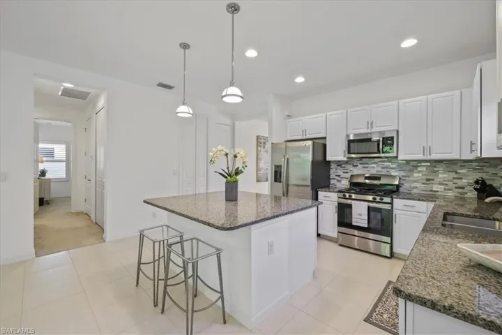 Kitchen featuring stainless steel appliances, a kitchen bar, white cabinetry, dark stone counters, and hanging light fixtures