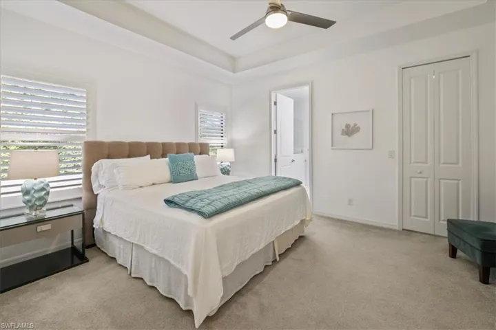 Bedroom featuring light colored carpet, a ceiling fan, and a tray ceiling