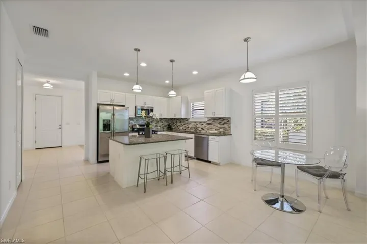 Kitchen with decorative light fixtures, white cabinets, stainless steel appliances, a breakfast bar area, and a kitchen island