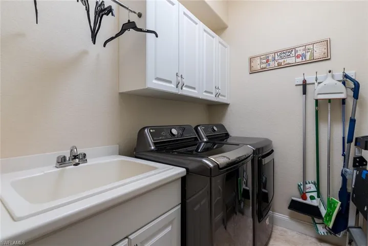 Clothes washing area featuring washing machine and dryer, cabinets, sink, and light tile patterned floors